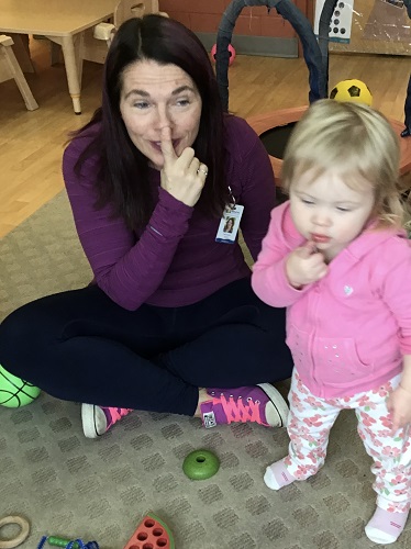 An infant and educator hold finger to mouth to say "shhh"