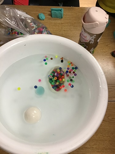 Clay boat filled with beads sinking in container of water