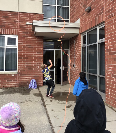 children getting a ball off a roof using a hula hoop and a skipping rope