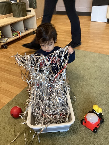 Infant exploring tinsel in a bucket
