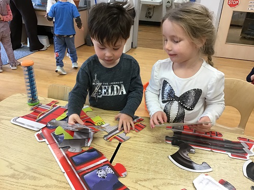 2 preschool children standing at the table building a puzzle together