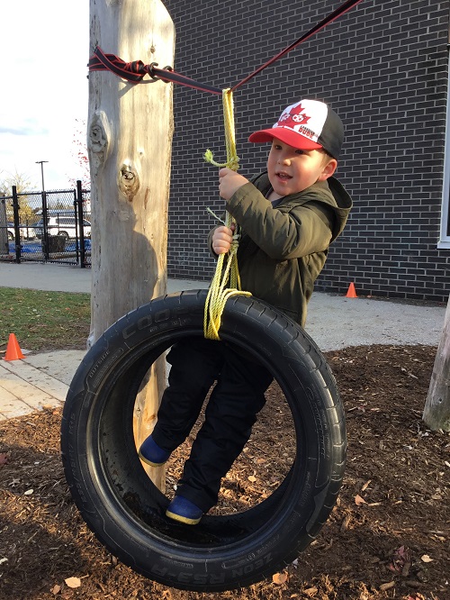 Preschool boy climbs up on the tire swing