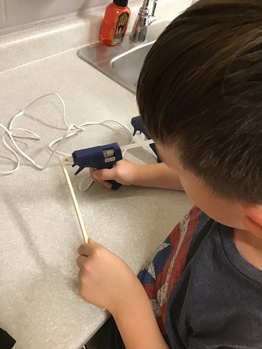A child using a hot glue gun to put glue on a chopstick