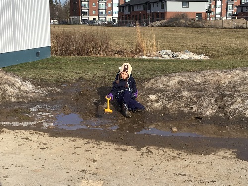 A child sitting beside a large puddle and a melting snow bank