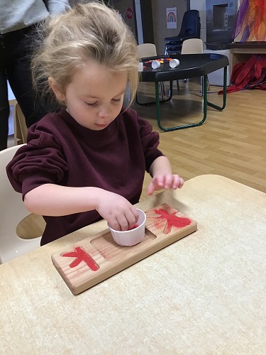 A child pinching sand from a paper cup and putting it on a letter plate