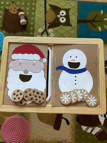 A painted Santa and Snowman on large pieces a cardboard and small cardboard circles made into snowflakes and cookies