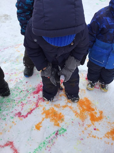 A child spray coloured water on the snow
