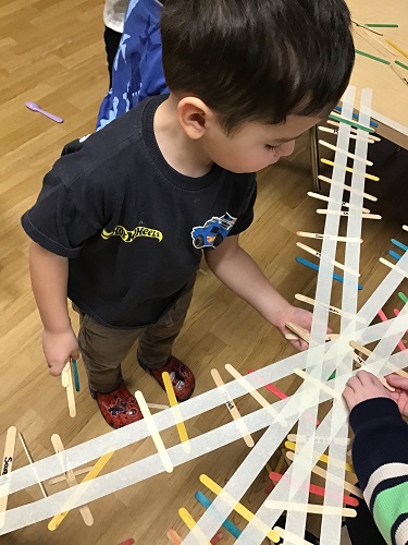 A child sticking popsicle sticks to tape to create a bridge