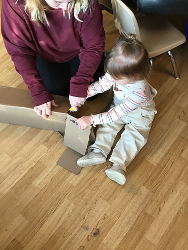 An educator and child usingchild safe cardboard cutters to cut a large piece of cardboard