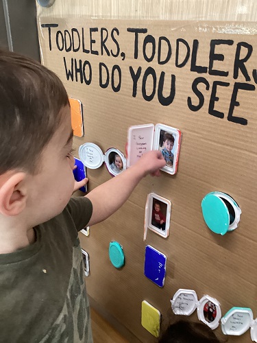 A child pointing to himself in a picture on the wall.