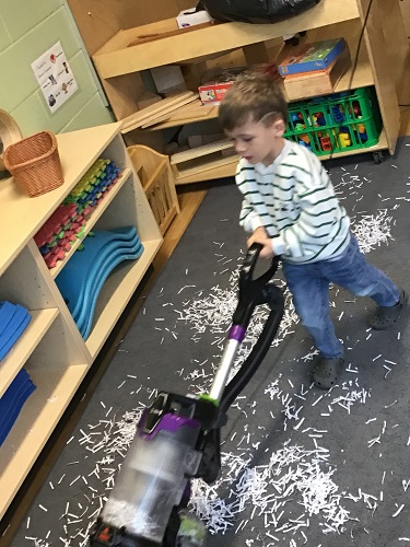 A child using a vacuum on the carpet in the classroom