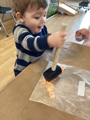 A child using a mallet to squish chalk in a ziploc bag
