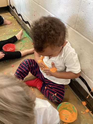 A child using his hands covered in chalk paint to create hand prints his shirt