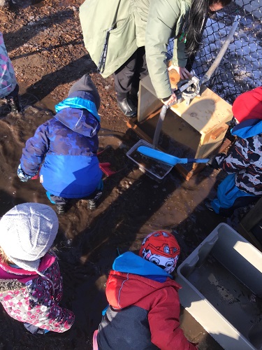 Children and an educator scooping water into a smaller bucket