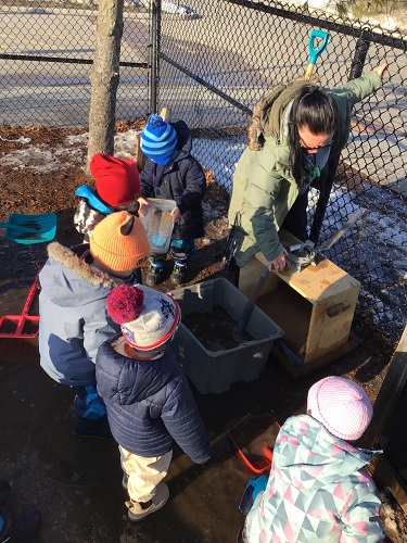 Children and an educator scooping water into the water pump bucket