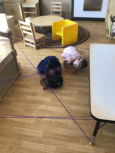 Children crawling under and through string tied around the table and climber
