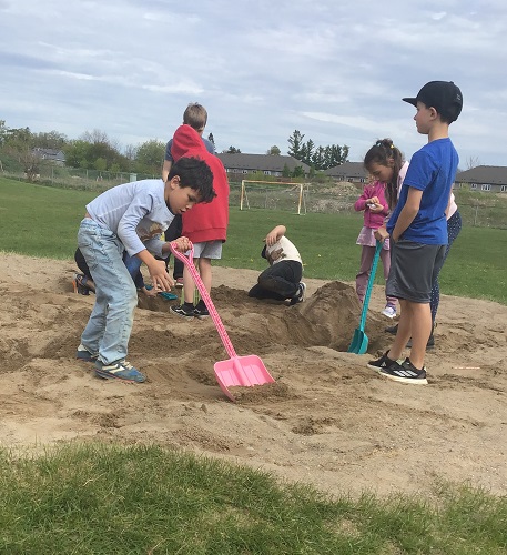 Children outside in the sand pit using large shovels