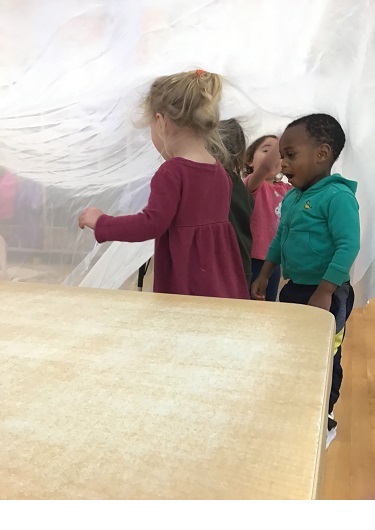 2 Toddler children underneath a fabric that is being raised by tables