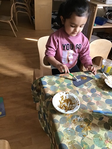 Preschool child sitting at the table holding a glue stick and placing glue on their paper