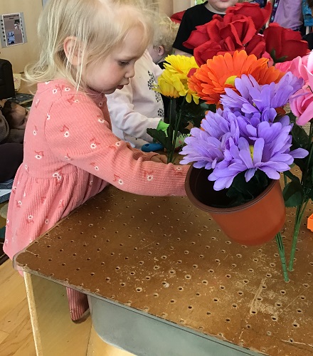 Toddler standing holding a bunch of flowers and looking at others