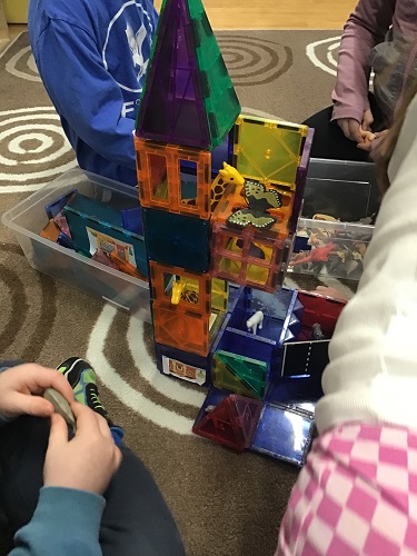 4 school age children sitting around a magnetic tower with animals and butterflies