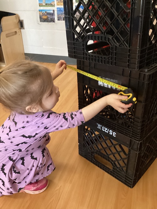 A preschool child using a measuring tape to measure crates