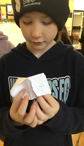 School Age 2 child standing with a cootie catcher in his hands looking at the cootie catcher