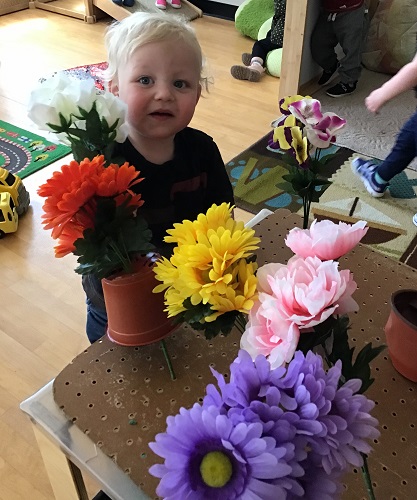 Toddler standing with a bunch of flowers smiling