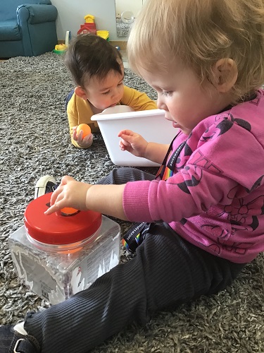 Two infants are playing with ping pong balls and putting them into bins.