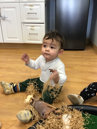 An infant is playing with shredded paper, some animals, and wood pieces.