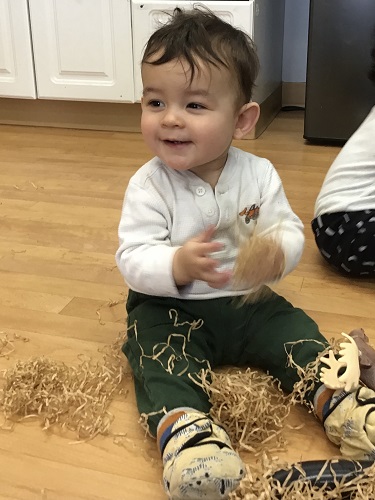 An infant is playing with some shredded paper.
