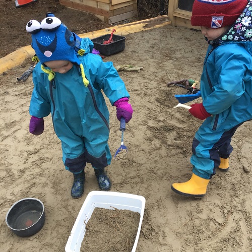 Preschoolers, dressed in their Muddy Buddies, are playing in the sandbox.