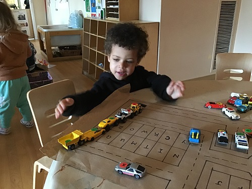A preschooler is lining cars up on a map.