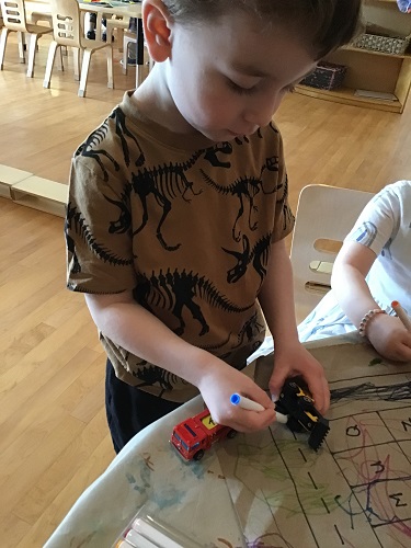 A preschooler is using a marker to colour on a cars tires.