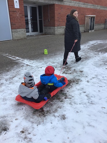 Educator pulling sled with 2 toddlers 
