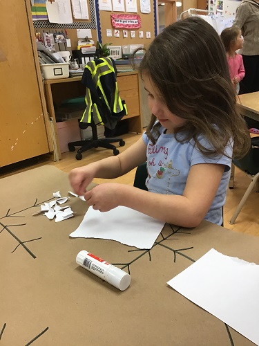 school-age girl gluing white pieces to snowflake 