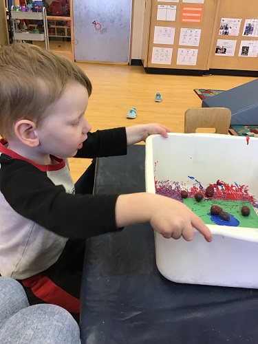 Toddler boy painting with acorns 