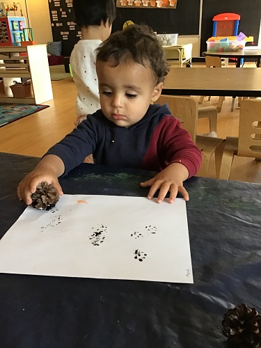 Toddler boy painting with a pinecone 
