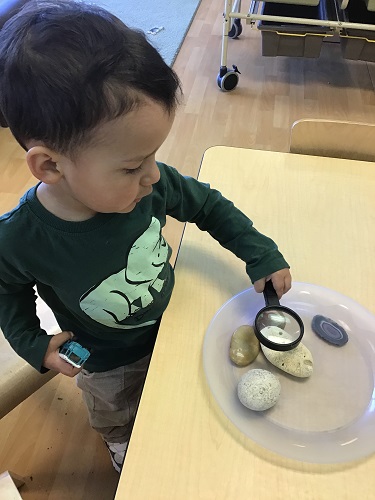 preschool child exploring rocks with magnify glass