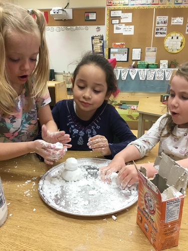 Group of school-age girls making a snowman with fake snow