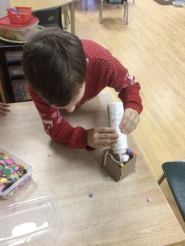 School-age boy decorating cardboard gingerbread house 