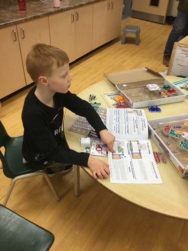 school-age boy using instruction books to build circuit 