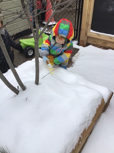 A preschooler is squirting paint into snow outside.