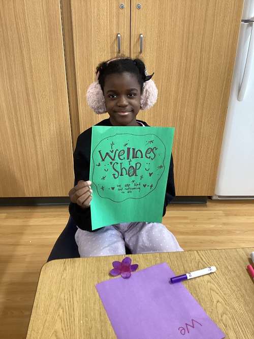 A school age child holding a sign that says "welcome to our wellness shop"