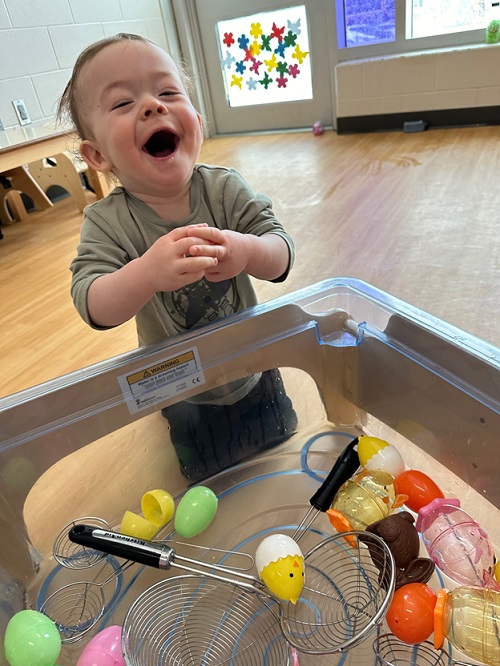 A child laughing while exploring with a scoop in water with plastic eggs.