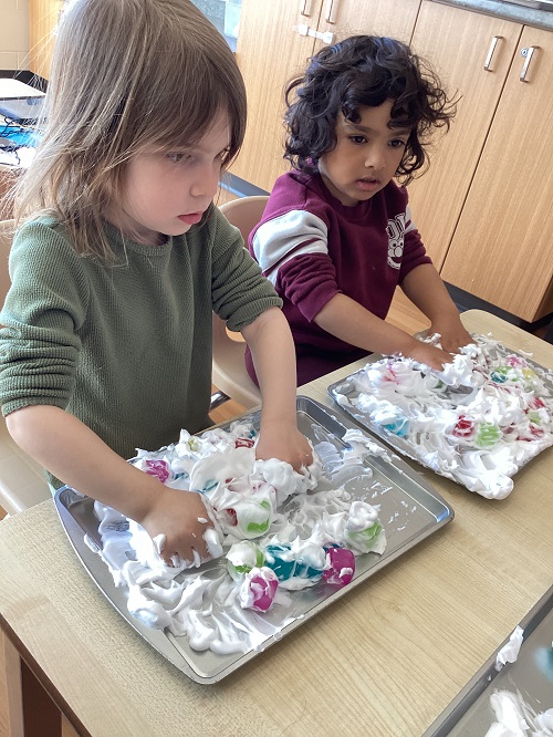 Two children exploring with shave foam and loose parts.