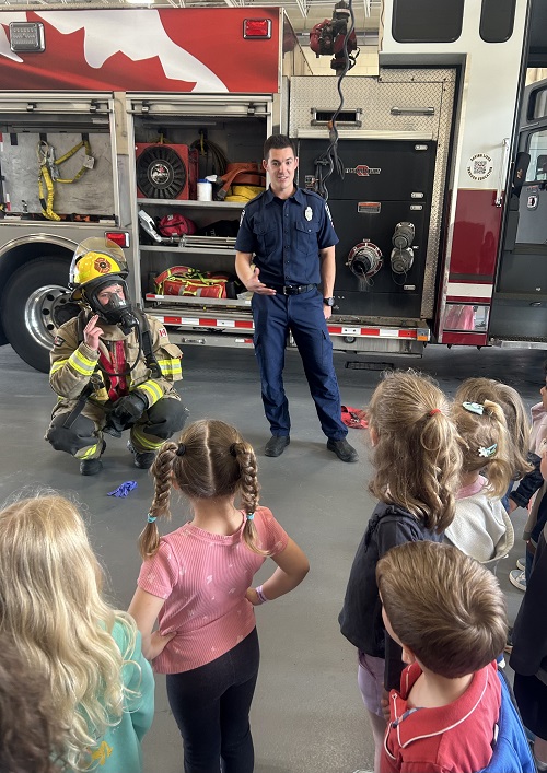 Two firefighters displaying and demonstrating how to use some of their gear.