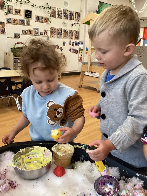 Children exploring with foam and dishes in the tuff tray.