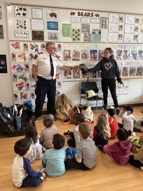 A firefighter and helper doing a demonstration for a group of children