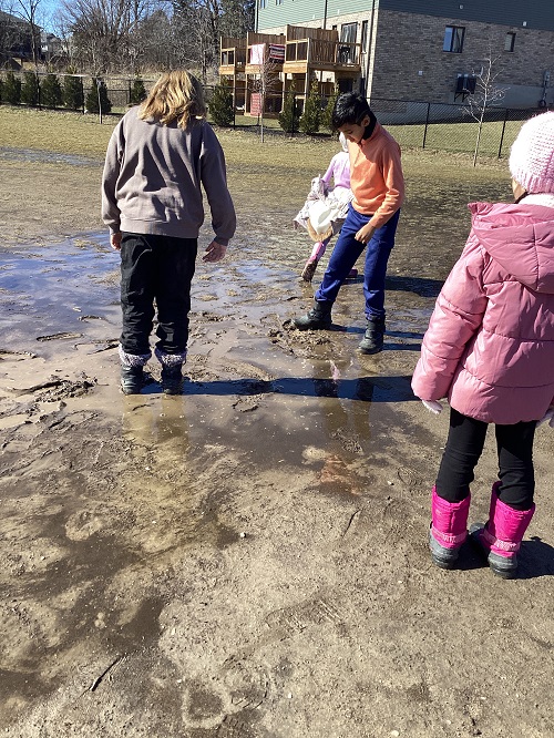 A small group of children walking through mud and observing the appearance.